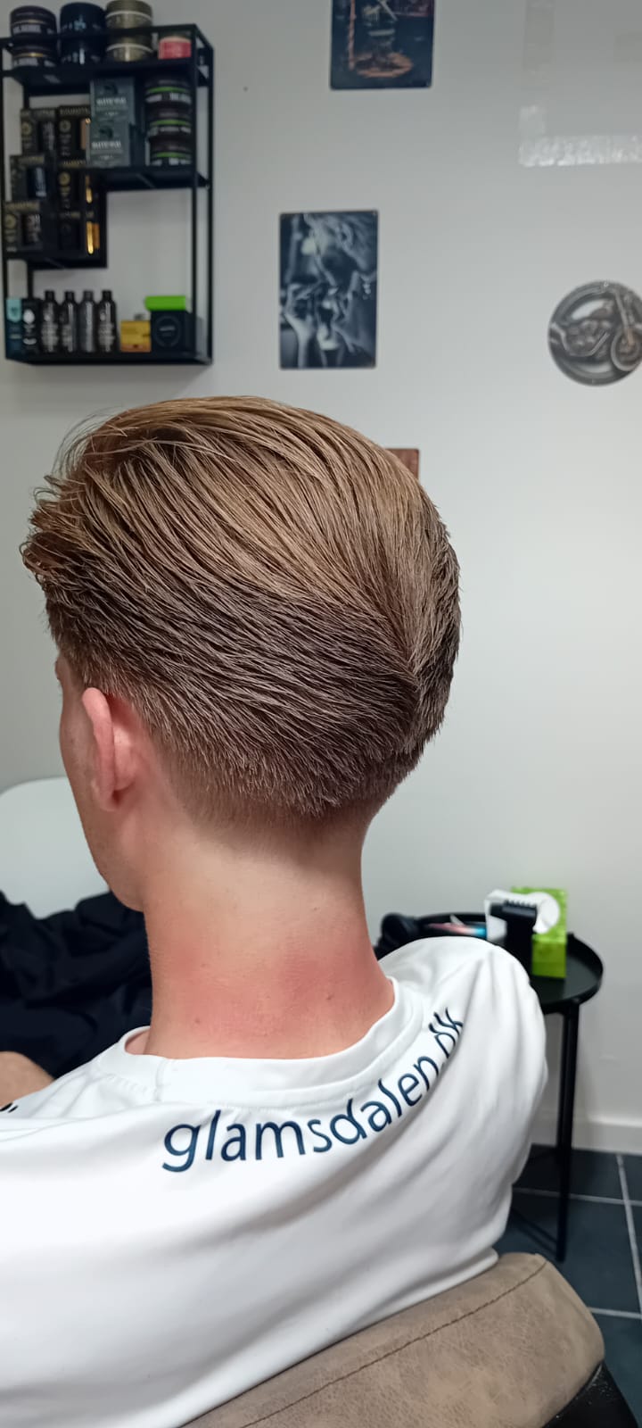 Slick back frisure med low fade i siderne på klient med blondt hår - herrefrisure set bagfra